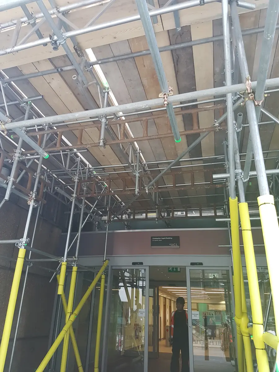 A scaffold built over a building entrance, with yellow guards