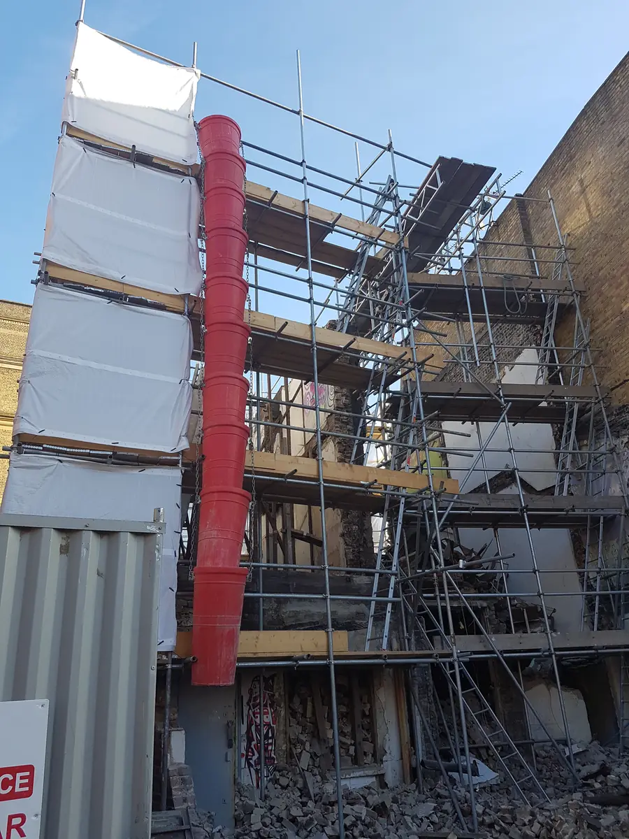 A red rubbish chute run down a scaffold on a strip-out