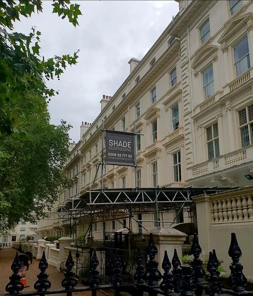 A white stucco-fronted London terrace wrapped in scaffold, with a Shade Scaffolding banner